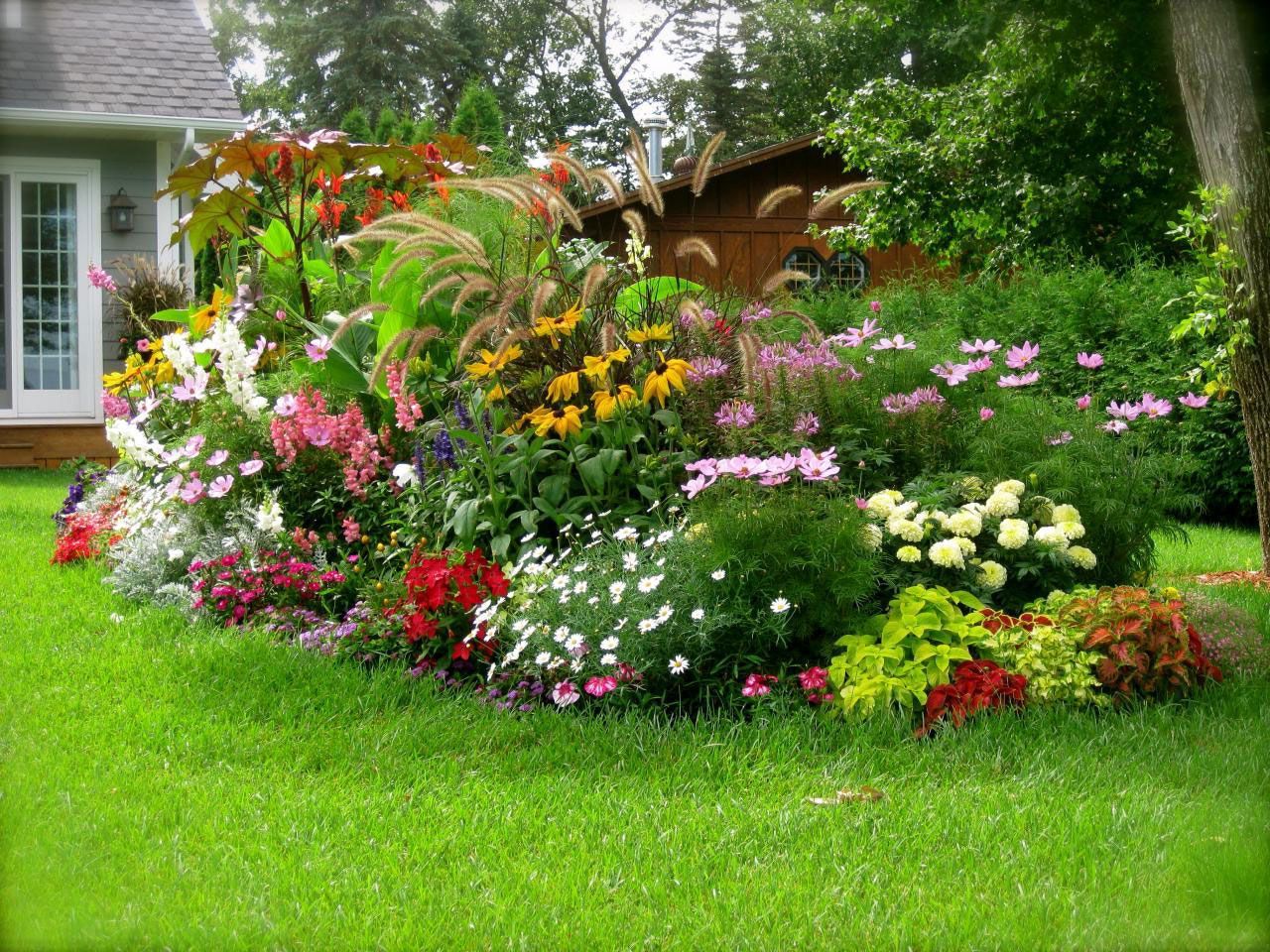 A garden filled with lots of flowers and plants in front of a house.