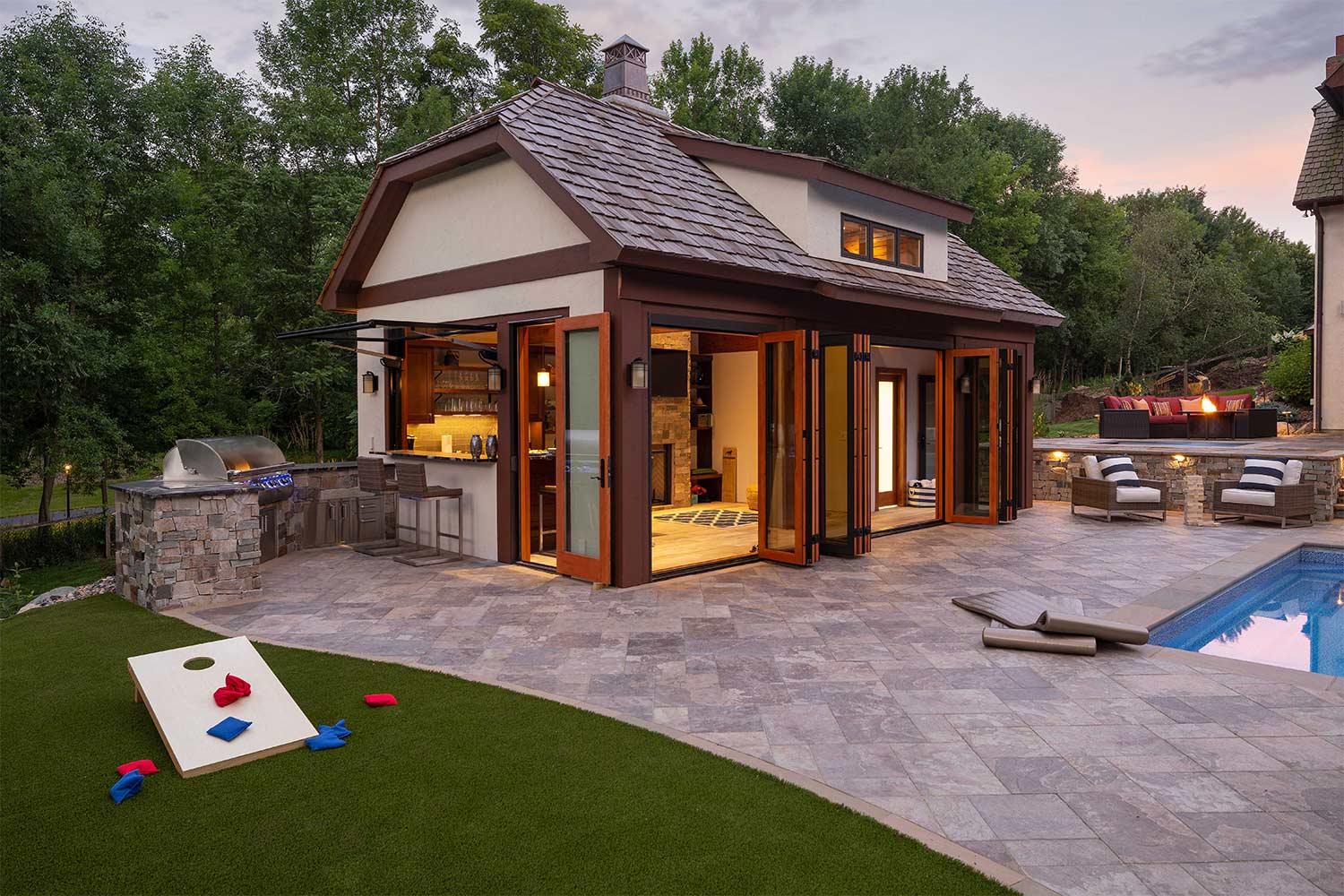 A house with a swimming pool and a patio with a game of cornhole on the grass.