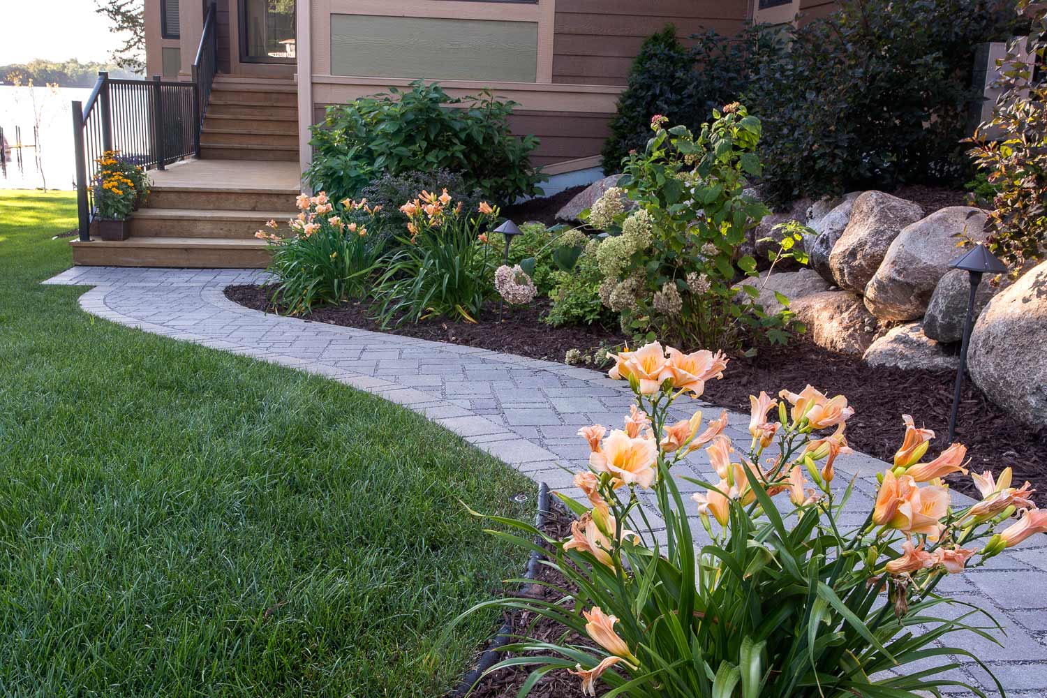 A brick walkway leading to a house with flowers in the foreground.