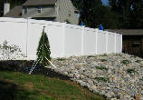 A white fence surrounds a rock wall in front of a house.