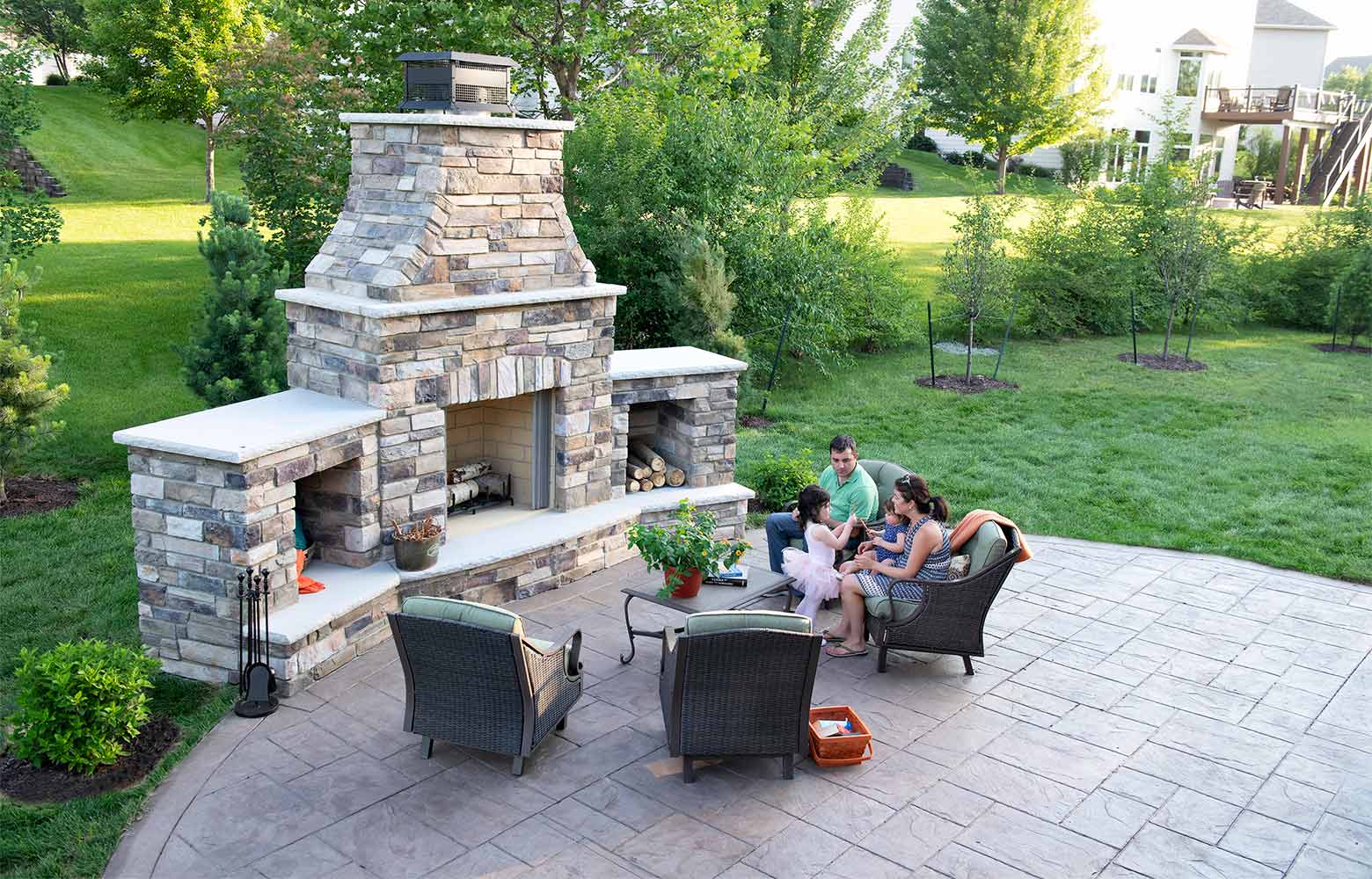 A group of people are sitting around a fireplace on a patio.