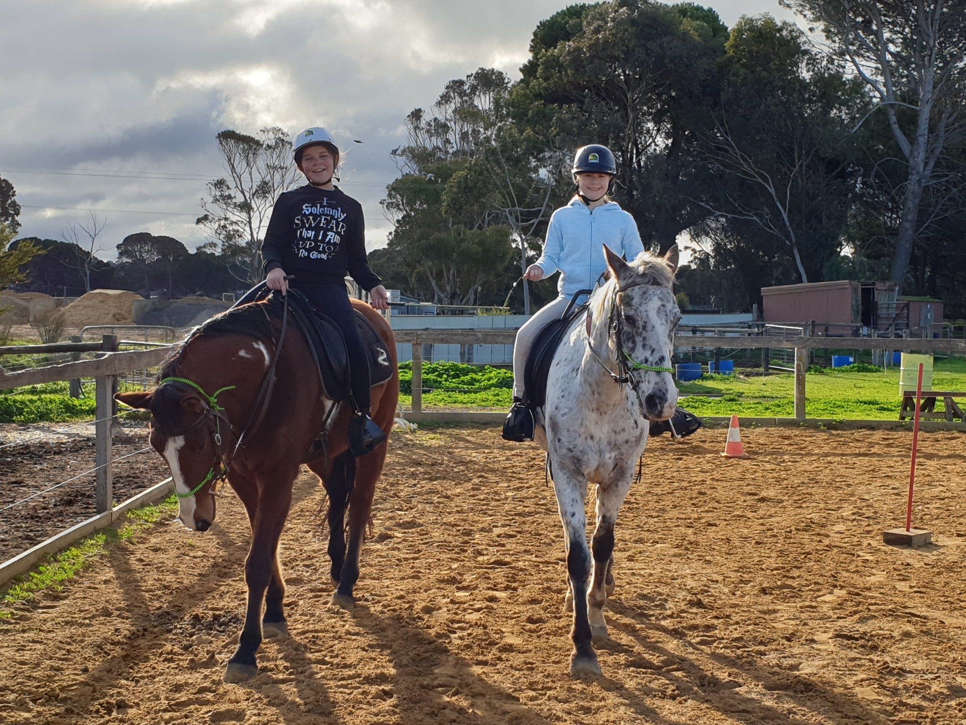 two students riding horses in the outdoor arena