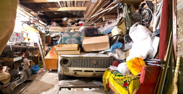 A car is parked in a garage filled with lots of junk.