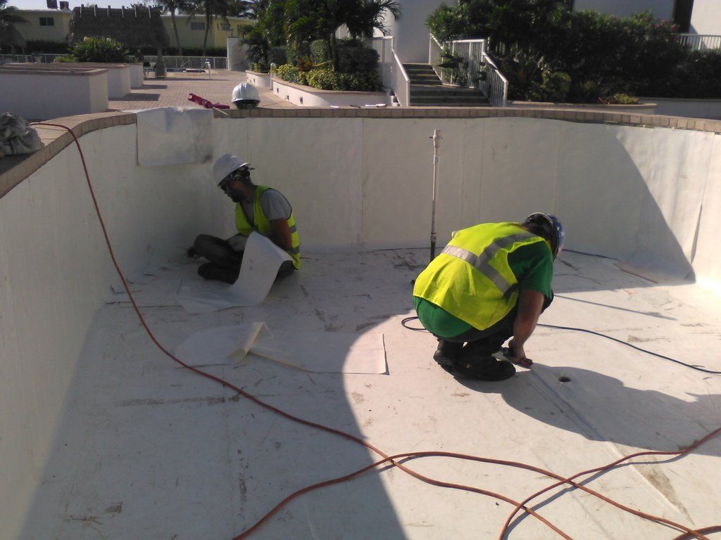two men in yellow vests are working on a swimming pool