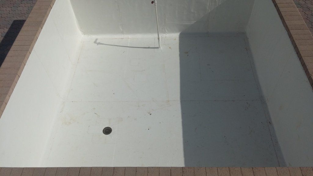 a white swimming pool is sitting on top of a brick patio .