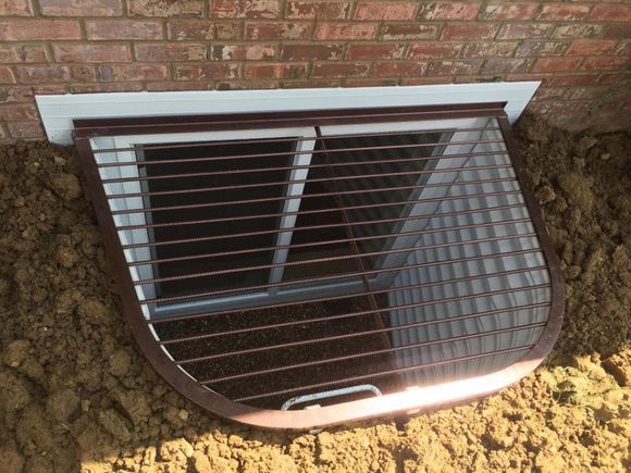Basement window well with metal grate below a brick wall, partly filled with dirt Basement window well with metal grate below a brick wall, partly filled with dirt
