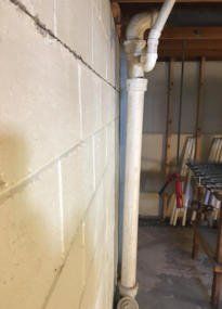 Basement utility area with white pipe against a cinder block wall and water stain on the floor Basement utility area with white pipe against a cinder block wall and water stain on the floor