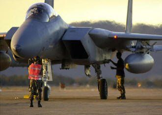 Two men are working on a fighter jet on a runway.