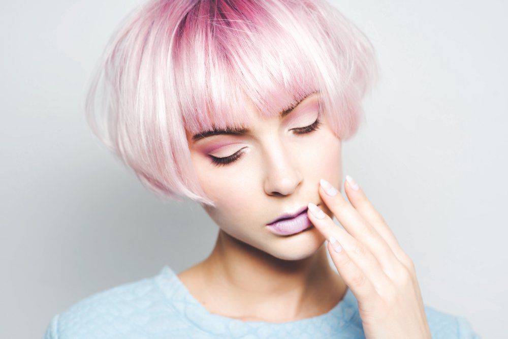 Eine Frau mit rosa Haaren und violetten Lippen bedeckt ihr Gesicht mit der Hand.