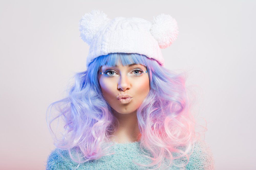 Eine Frau mit rosa und blauen Haaren trägt einen weißen Hut und wirft einen Kuss zu.