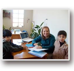 Una mujer está sentada en un escritorio con dos niños y una computadora portátil.