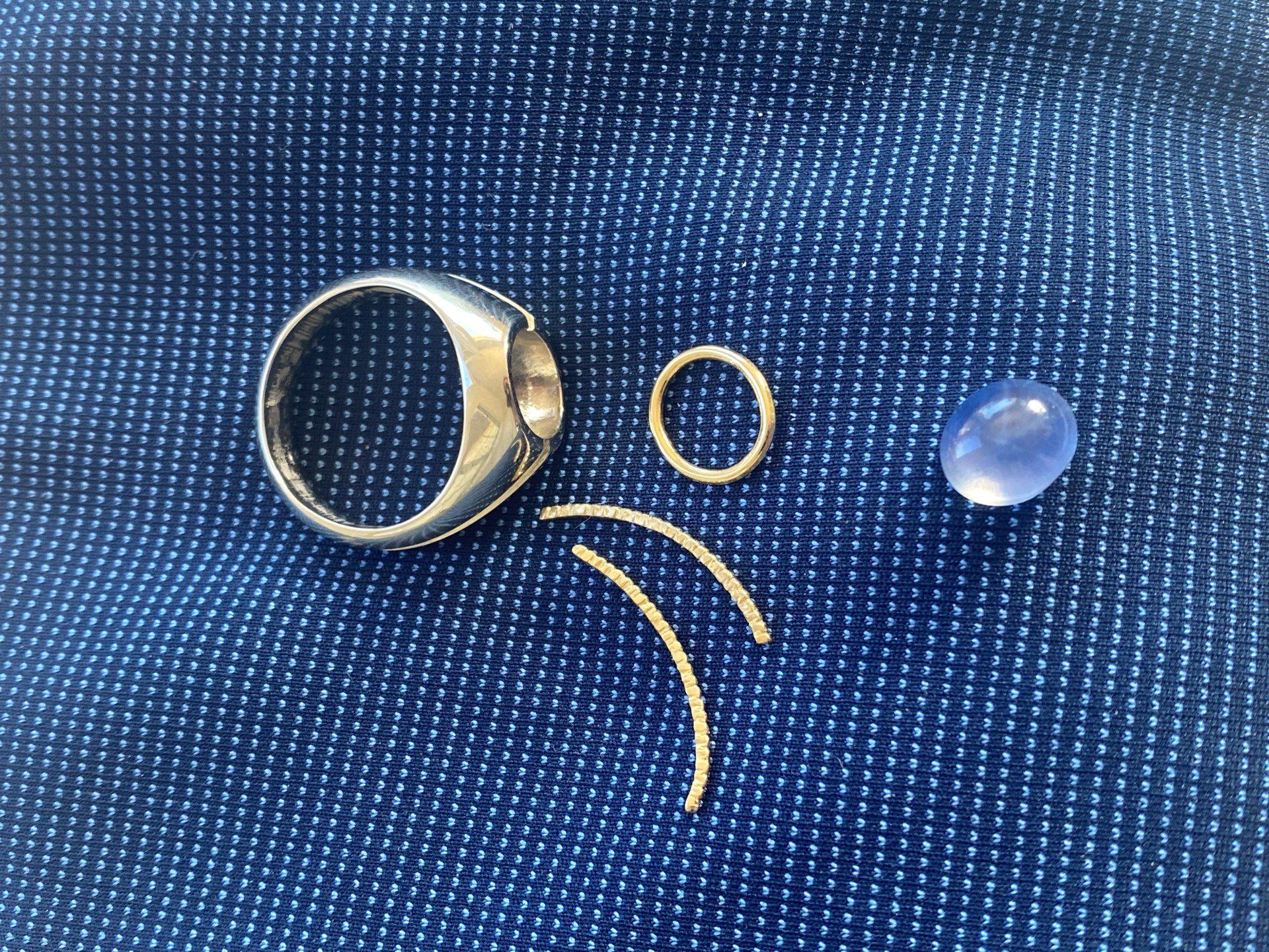 Silver ring and jewelry parts on blue denim. A blue gemstone sits on the right.