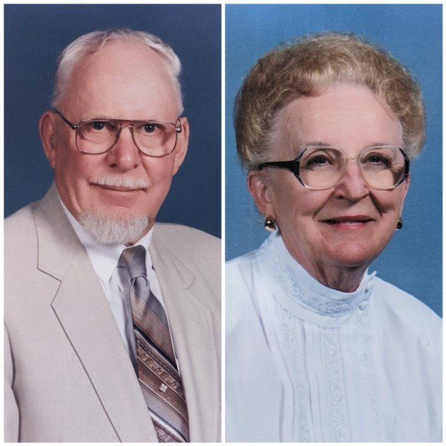 A couple, older with glasses, in formal attire. Man: light suit, goatee. Woman: white blouse, short hair.