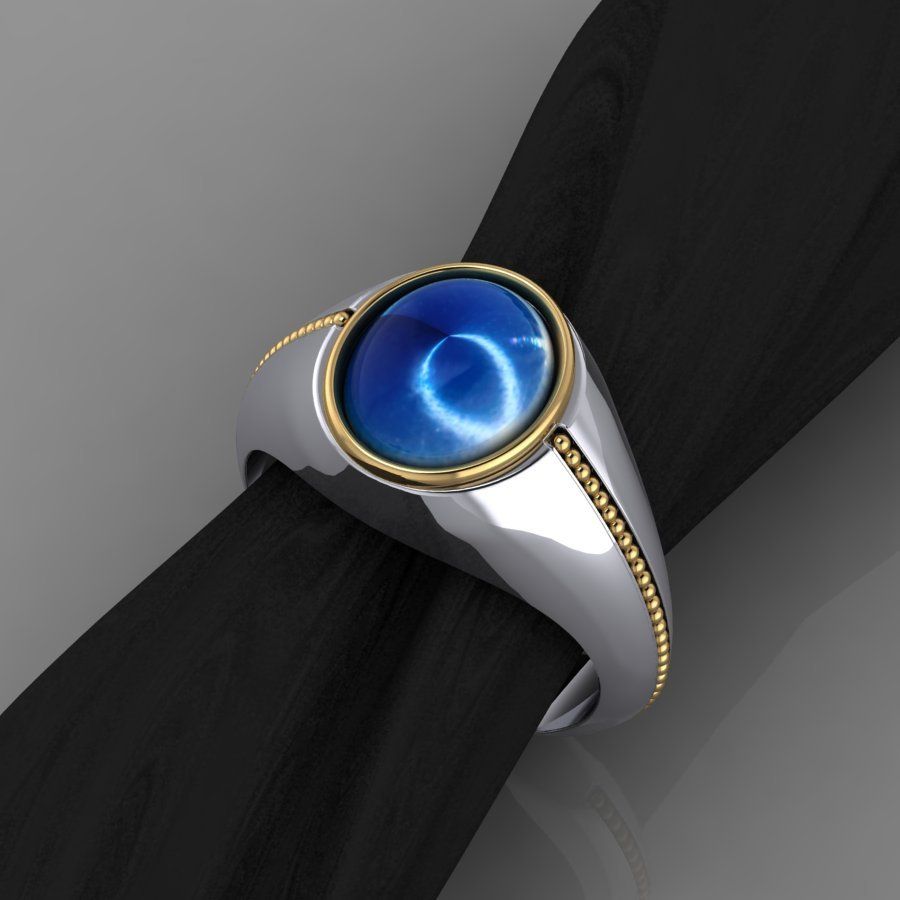 Blue and silver custom jewelry design in Colorado springs, CO Silver and gold ring with a blue cat's eye stone set on a black surface.