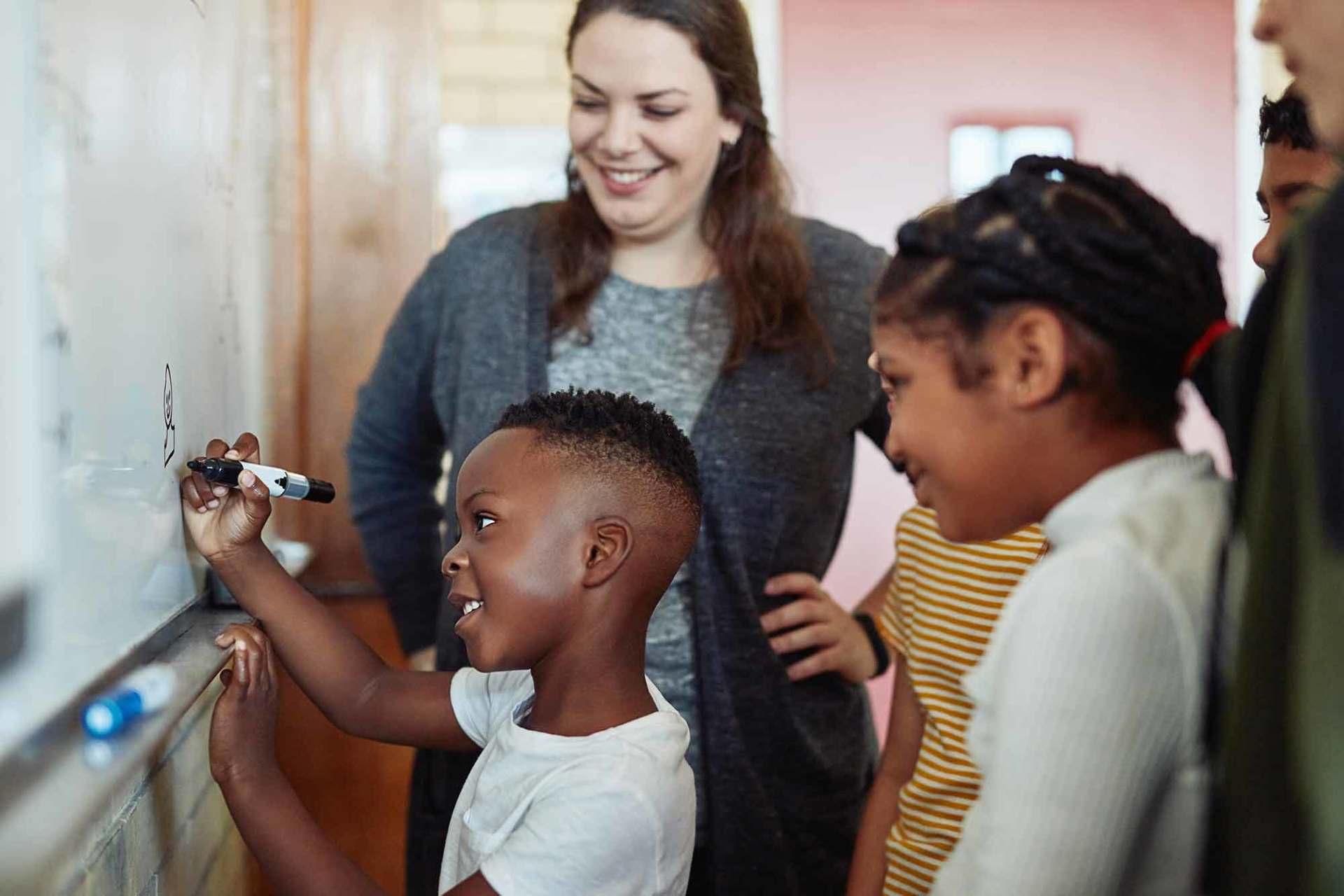 Shot of a group of young children writing on a board during a lesson with their teacher in a classroom