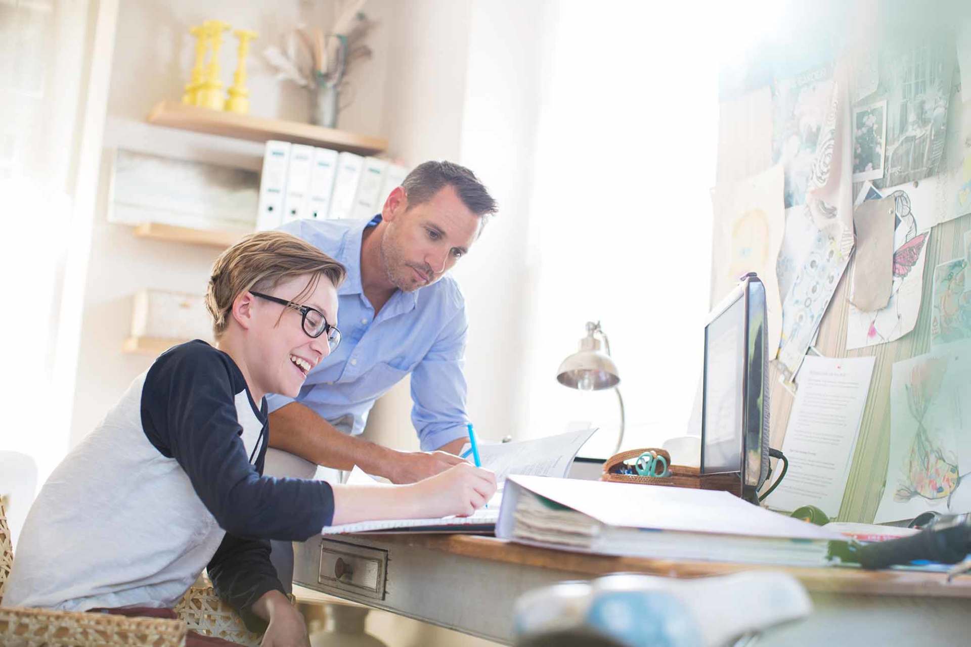 Father helping teenage son doing his homework in room