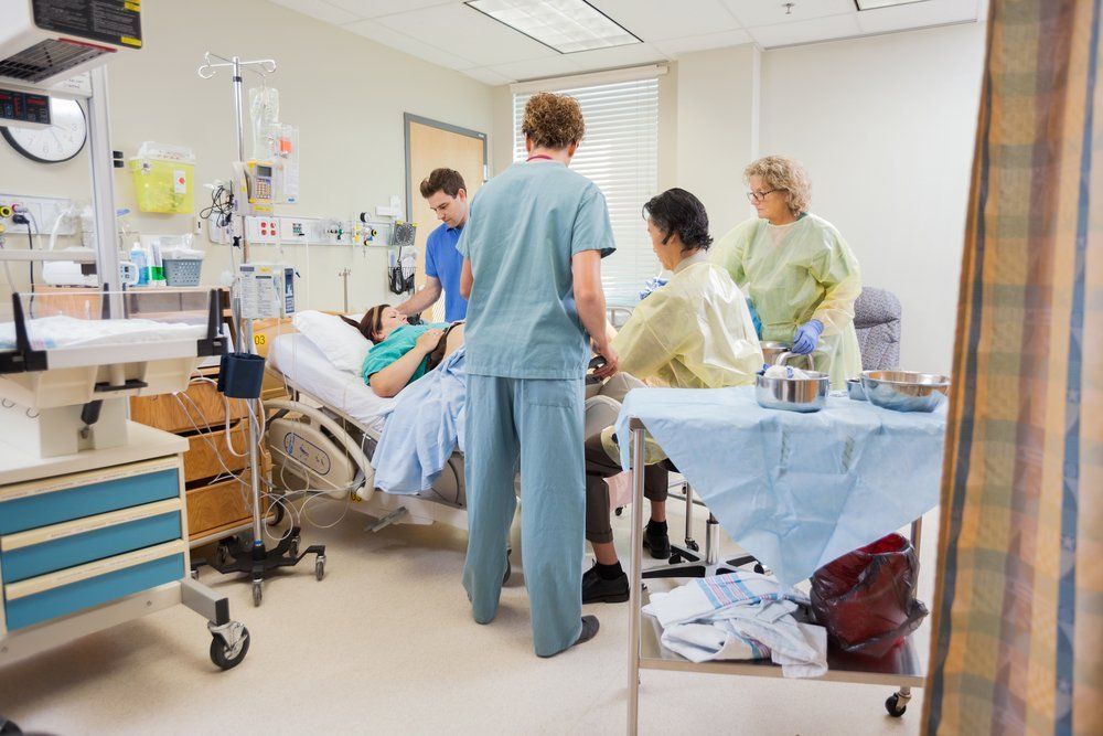 Medical team operating pregnant woman while husband standing by in hospital room