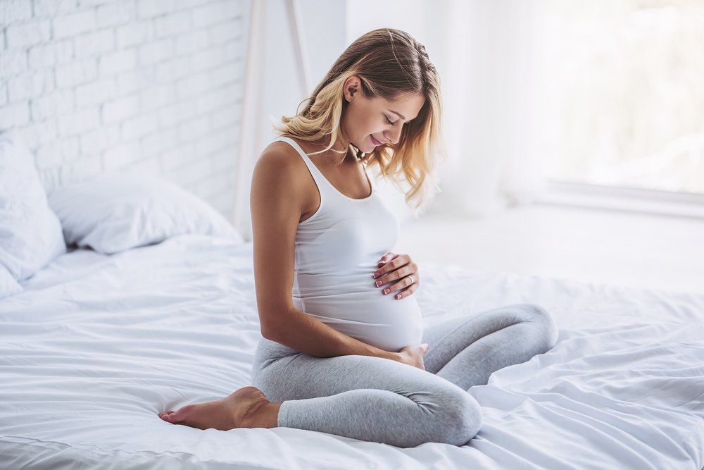 mother sitting on a bed and holding her pregnant stomach