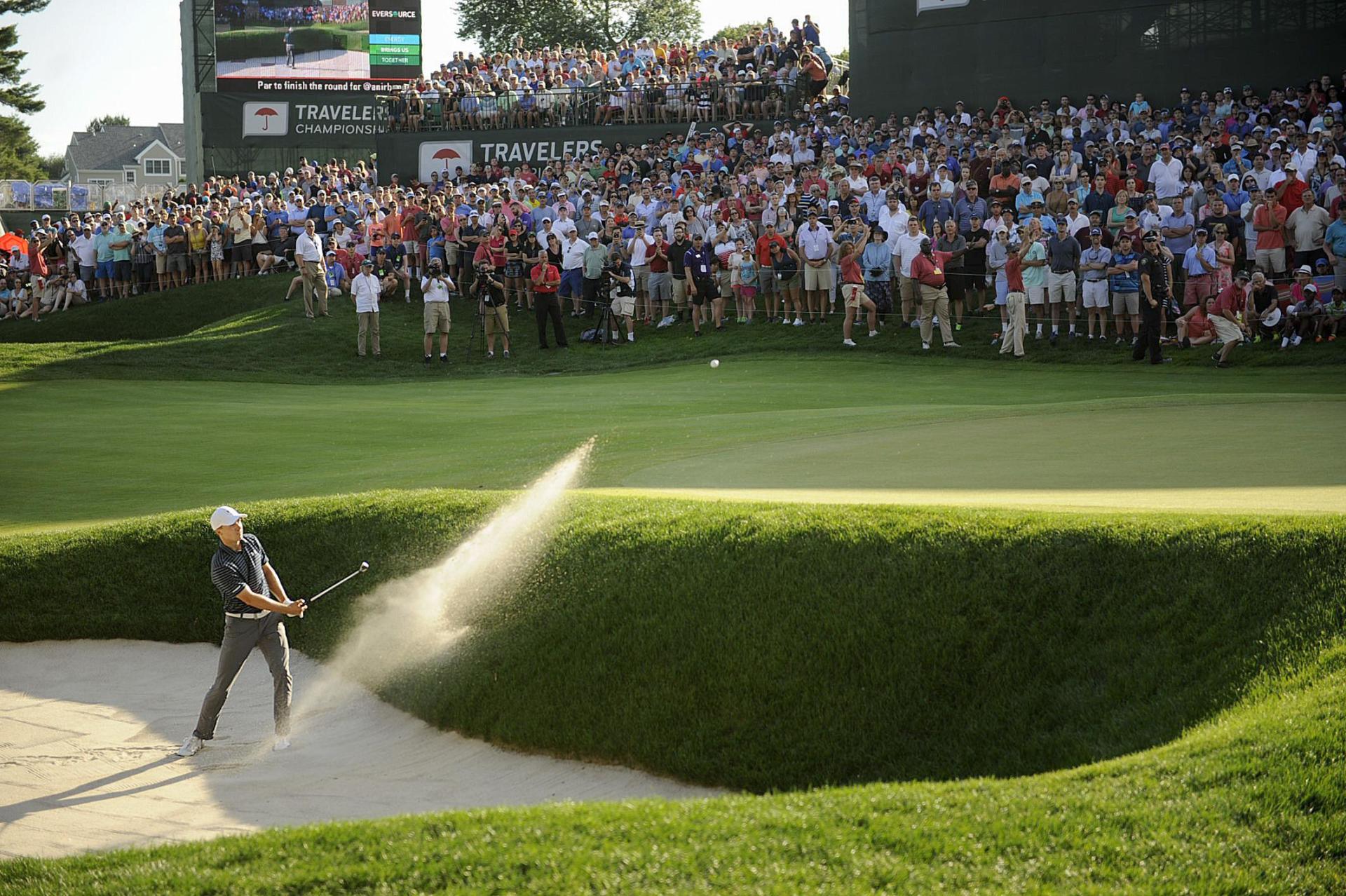 A man is hitting a golf ball out of a bunker on a golf course.