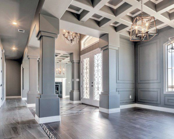 Elegant entry hall with gray paneled walls, wood floors, coffered ceiling, and hanging chandeliers