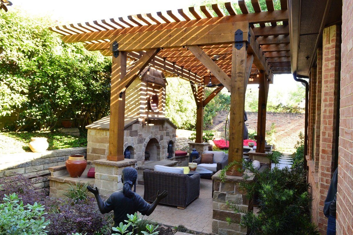 Outdoor patio with stone fireplace, wooden pergola, and brick columns in a landscaped garden