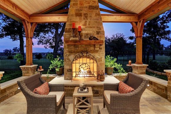 Covered outdoor patio with stone fireplace, wicker seating, and warm lighting at dusk