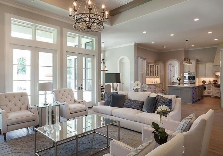 Bright open-concept living room with white furniture, glass coffee table, and adjoining kitchen