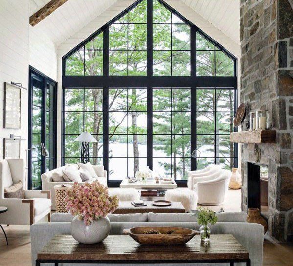 Bright modern living room with vaulted windows, stone fireplace, and neutral seating overlooking trees and water