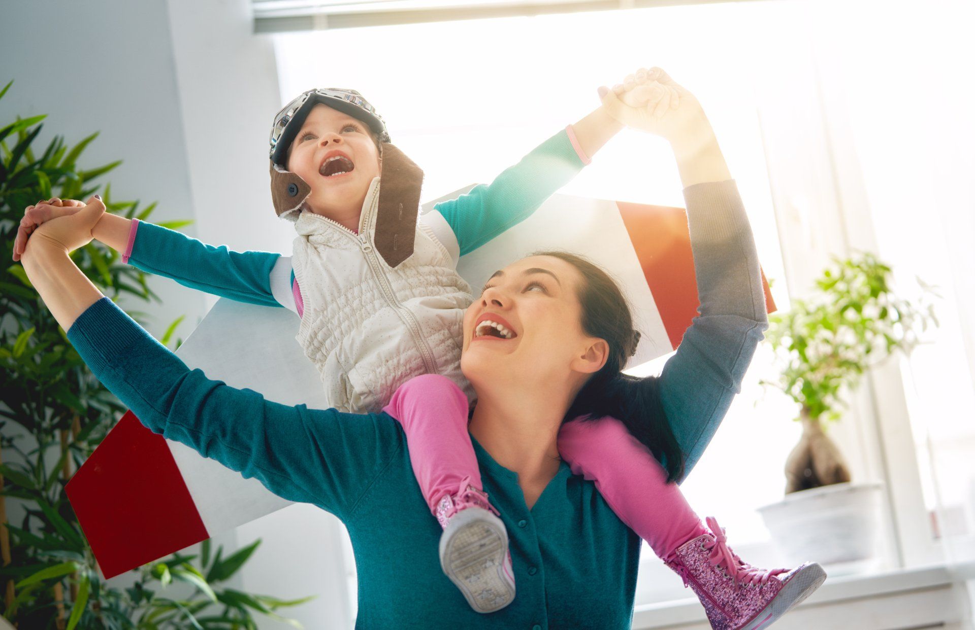 Woman carrying a laughing child on her shoulders in a bright room with colorful shopping bags