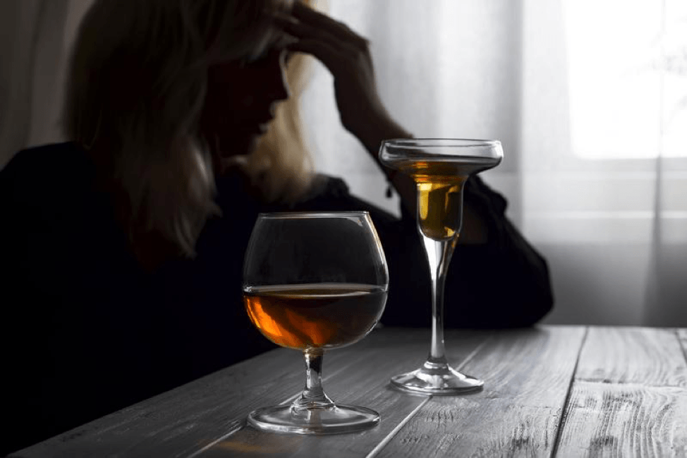 A woman is sitting at a table with two glasses of alcohol.