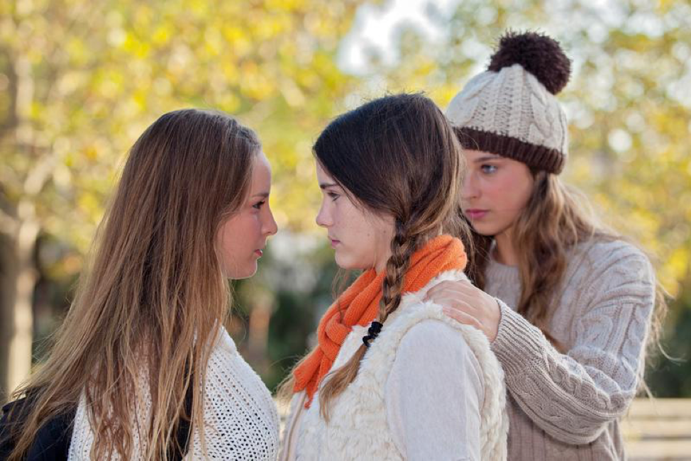 Three young women are standing next to each other in a park.