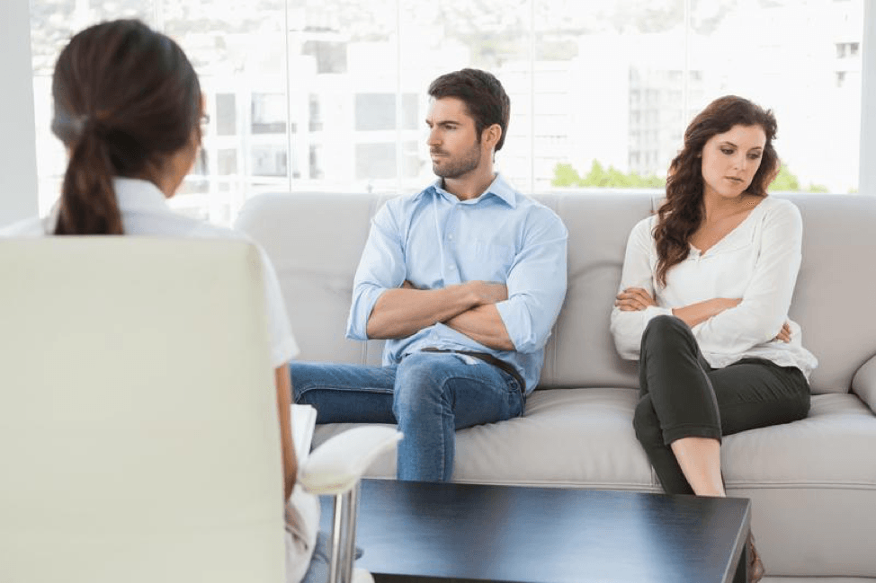 A man and a woman are sitting on a couch talking to a woman.