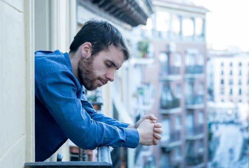 A man in a blue shirt is looking out of a balcony.