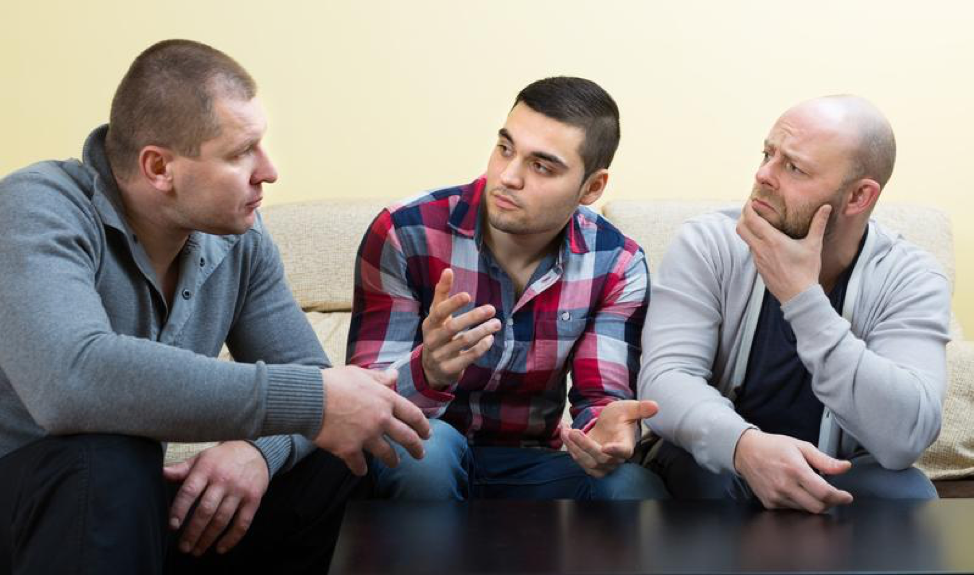 Three men are sitting at a table talking to each other.