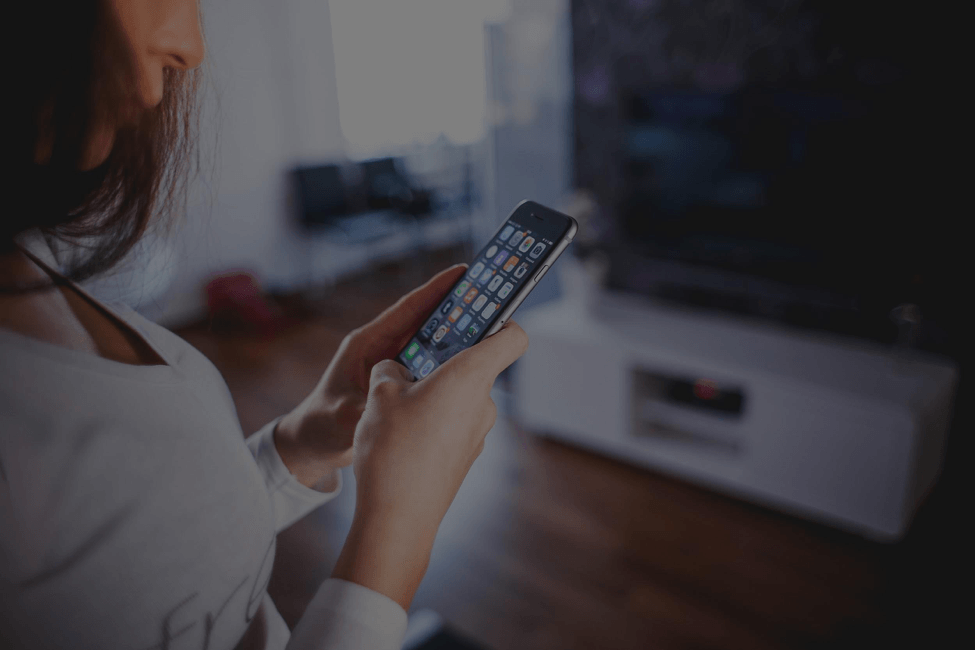 A woman is holding a cell phone in her hands in a living room.