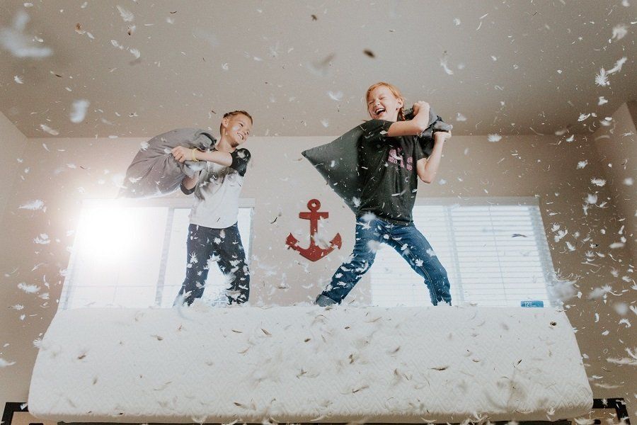 Two children are having a pillow fight on a bed.