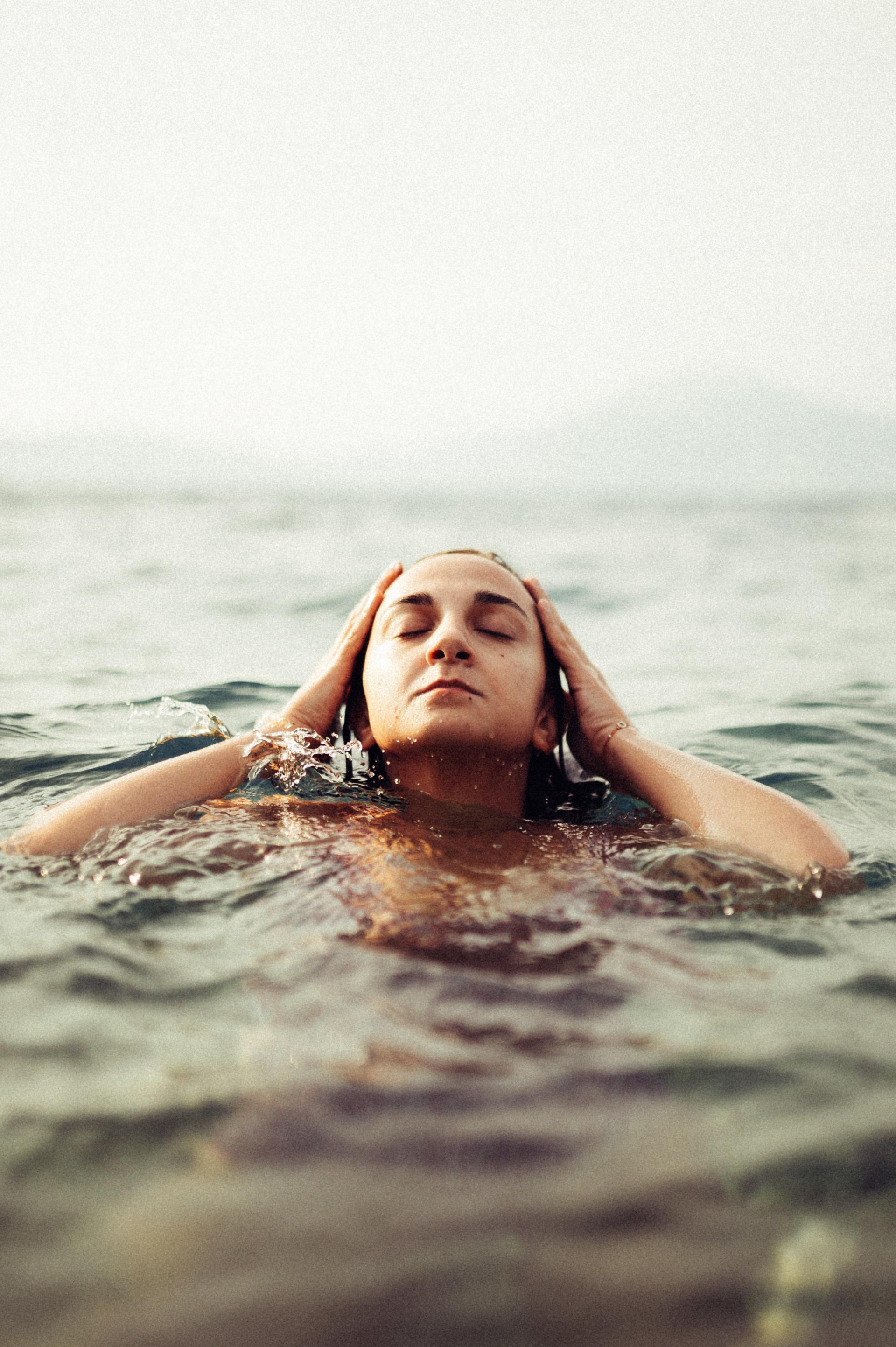 A woman is swimming in the ocean with her eyes closed.