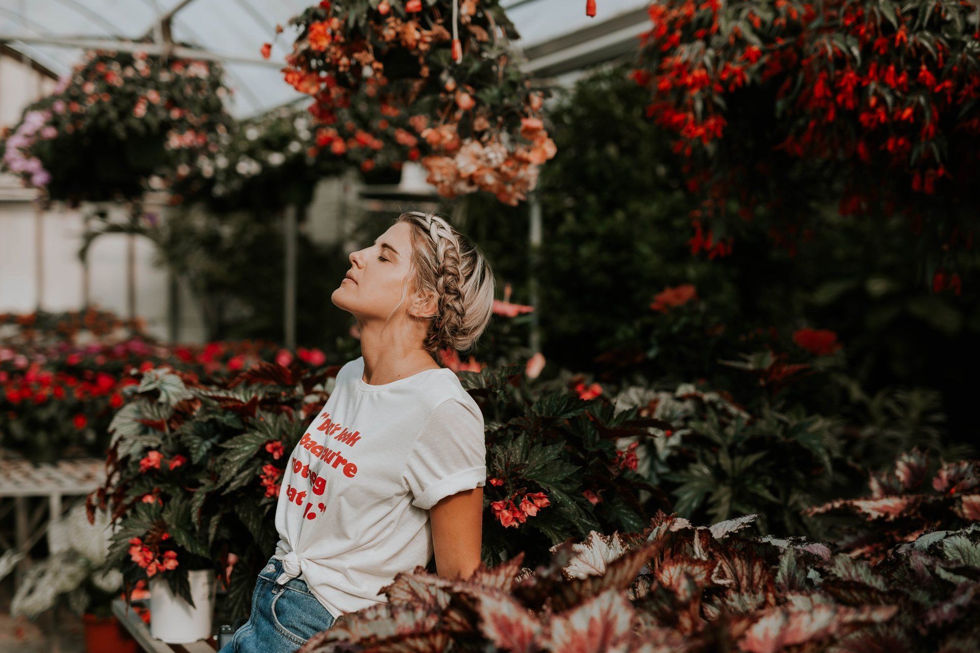 A woman is sitting in a greenhouse surrounded by flowers.