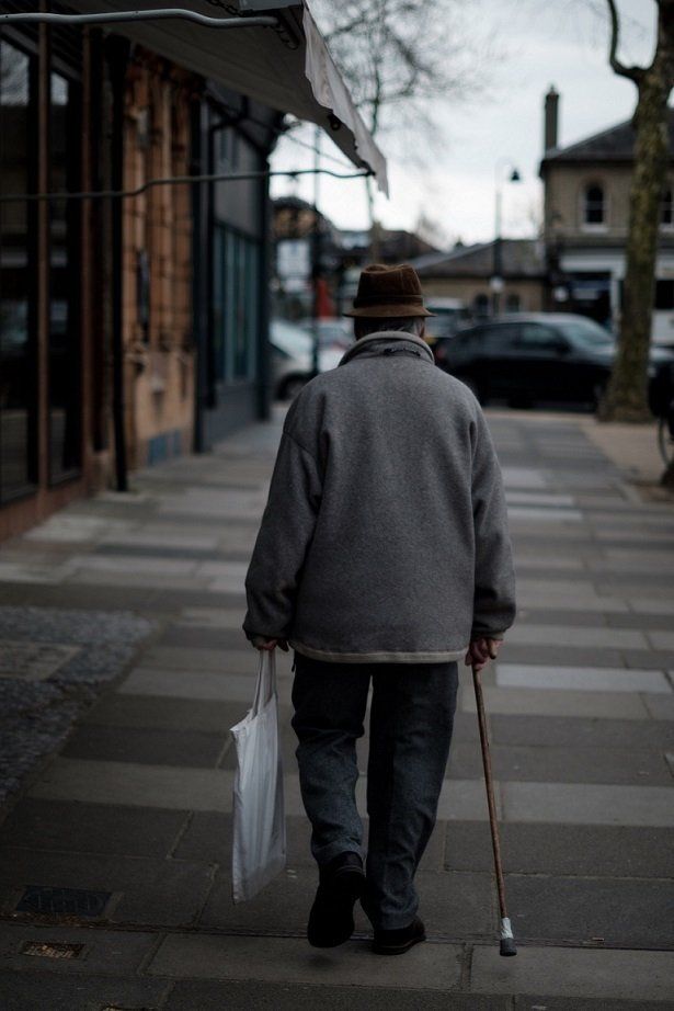 A man is walking down a sidewalk with a cane and a bag.