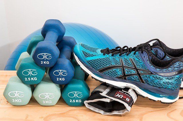 A stack of dumbbells , a pair of shoes , and a pair of gloves on a wooden table.