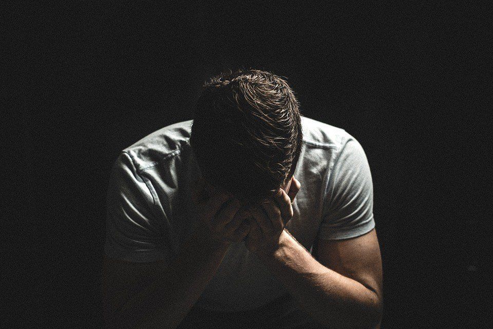 A man is covering his face with his hands in a dark room.