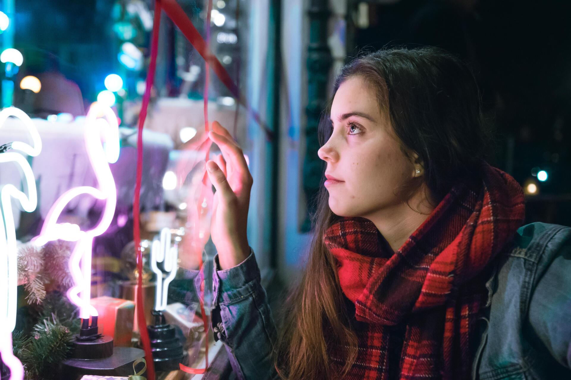 A woman is looking through a window at christmas lights.