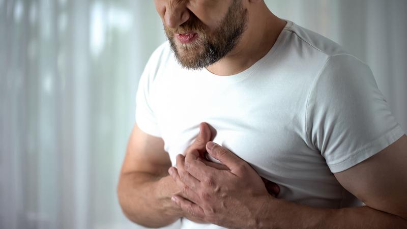 A man with a beard is holding his chest in pain.