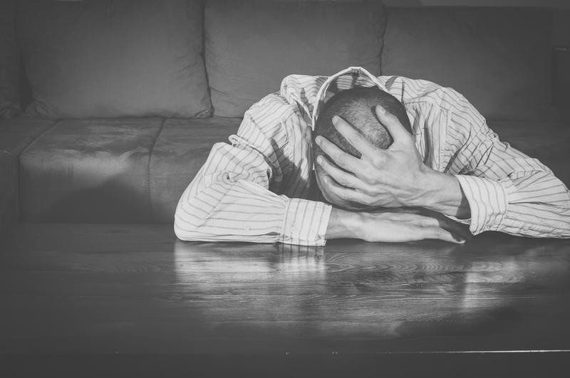 A man is laying on a couch covering his face with his hands.