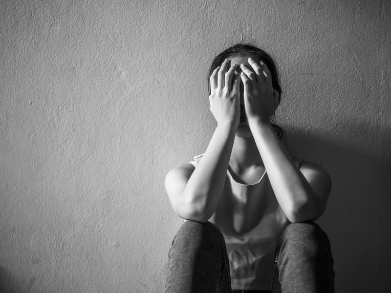 A woman is sitting on the floor covering her face with her hands.