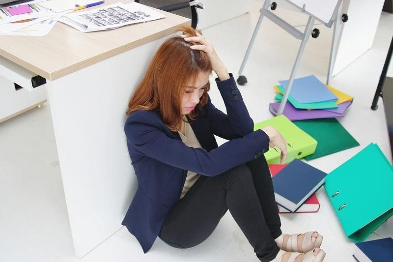 A woman is sitting on the floor in a messy office.