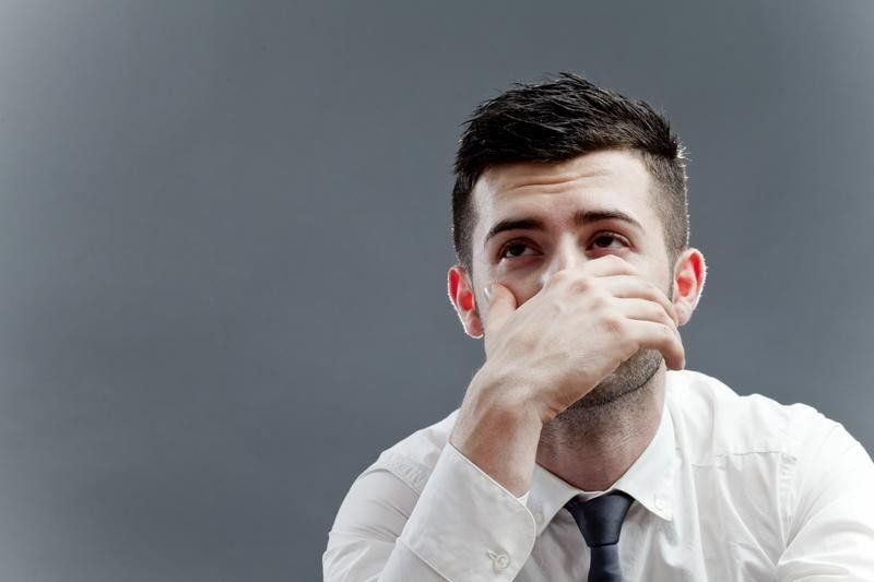 A man in a white shirt and tie is covering his mouth with his hand.