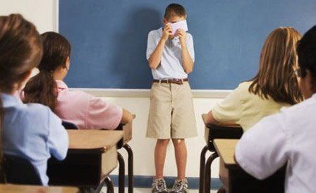 A boy covering his face with a piece of paper in a classroom