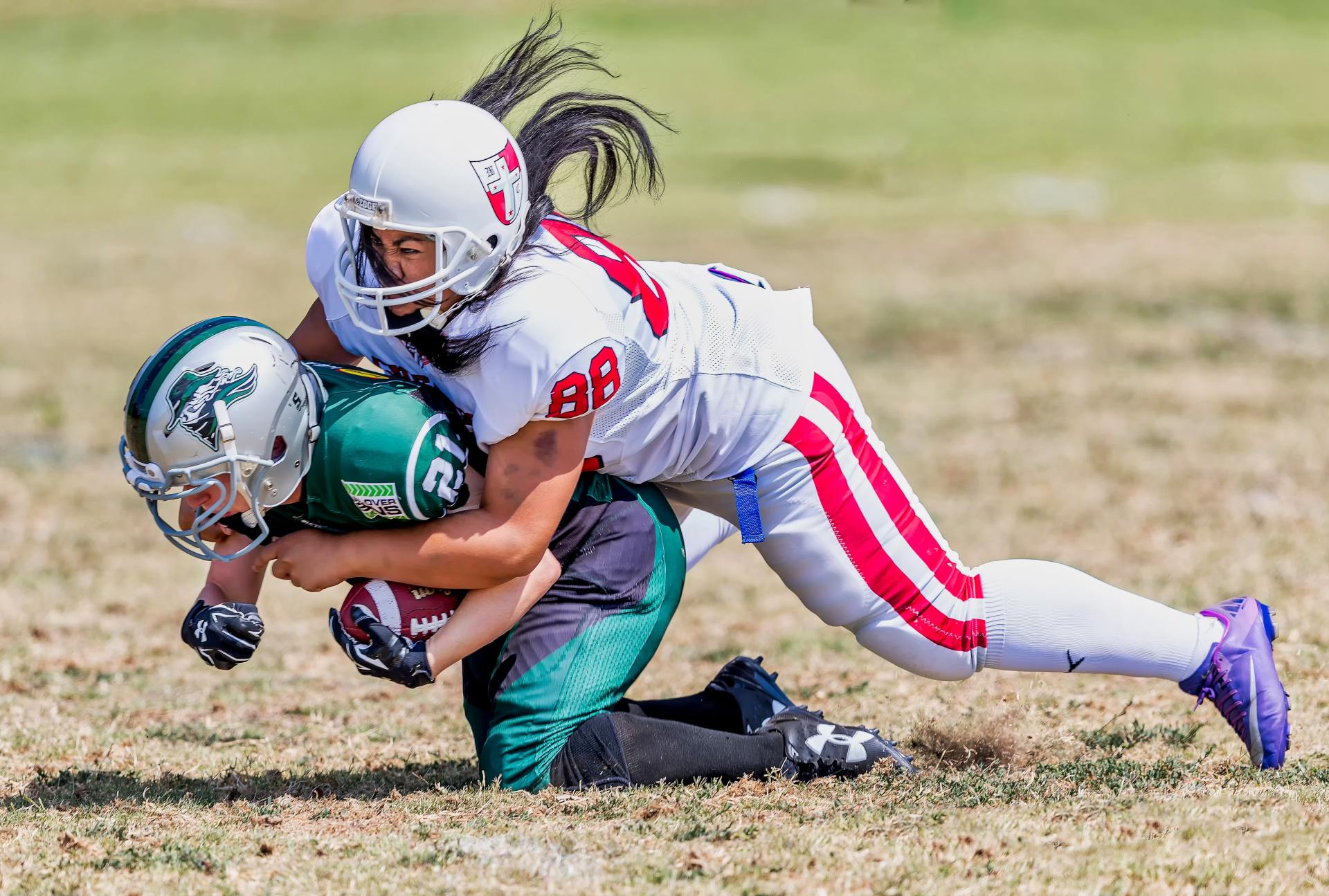 Two young girls are playing a game of football on a field.