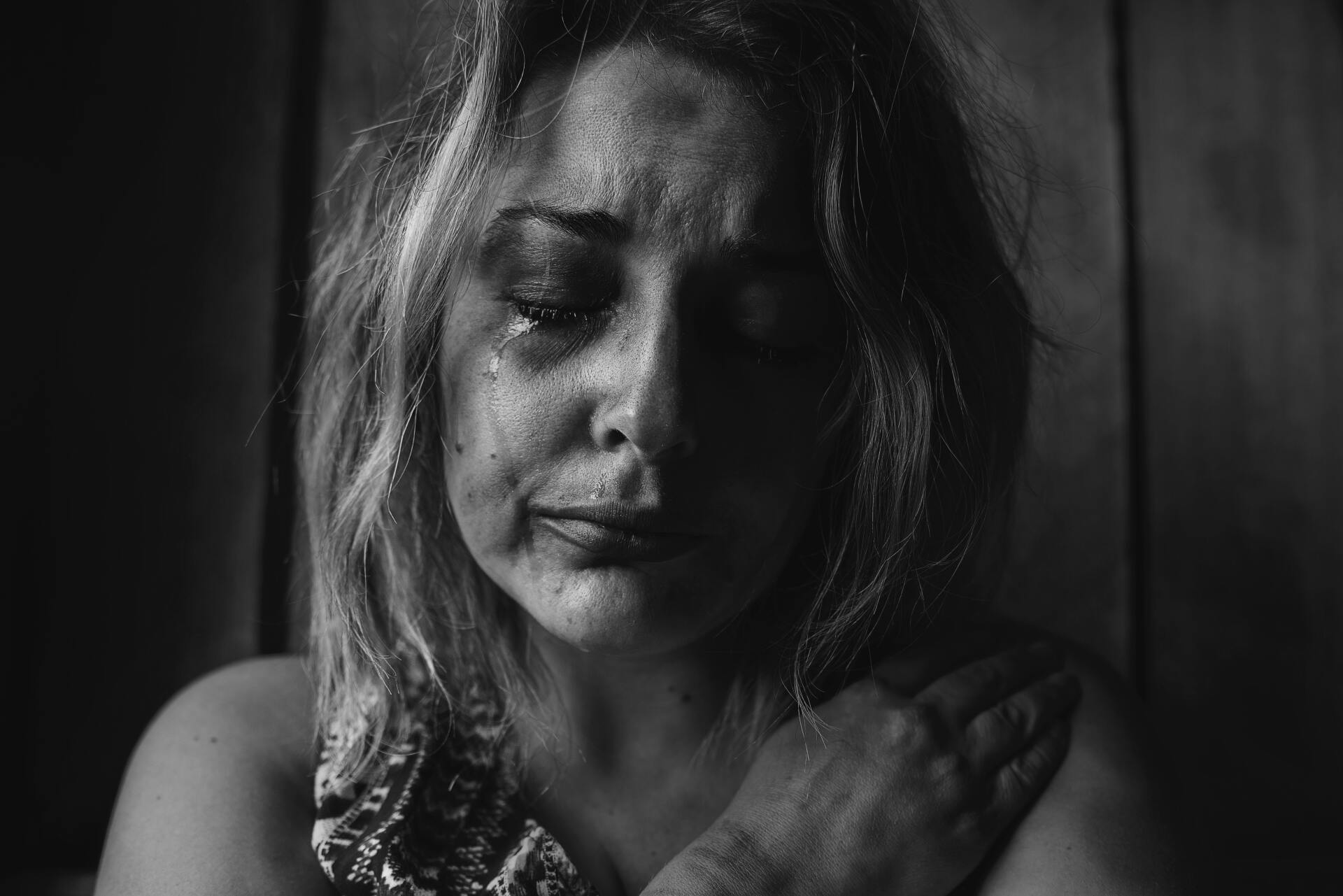 A woman with a bruise on her face is crying in a black and white photo.